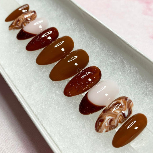 Load image into Gallery viewer, Short almond French tip press-on nails in various shades of brown with delicate glitter shimmer and a marble effect pattern.