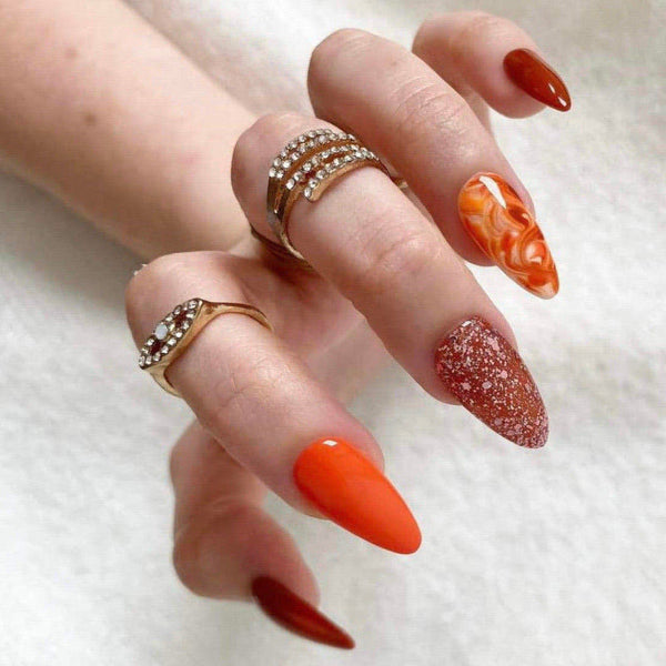 Load image into Gallery viewer, Hand wearing long almond press-on nails in tones of orange and brown, as well as multiple rings.