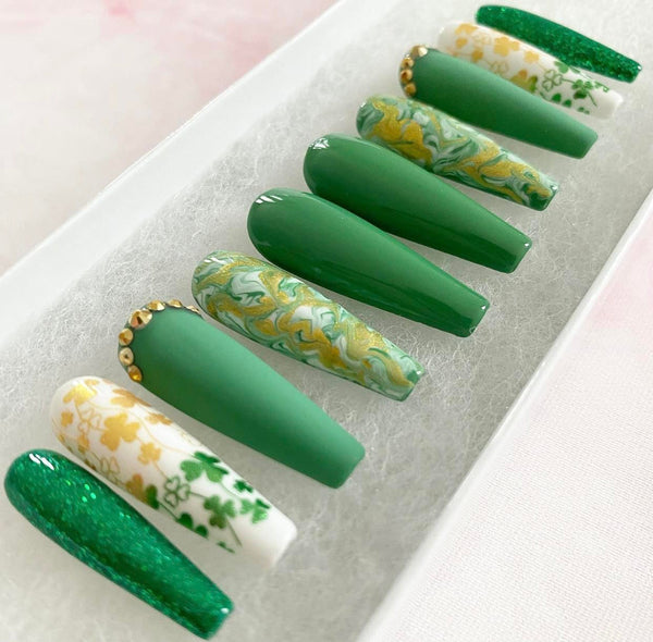 Load image into Gallery viewer, St Patrick's Day press-on nails in green and gold with a shamrock design, gold rhinestones, and gold-green marble effect design, in a long coffin shape, displayed in a white presentation box.