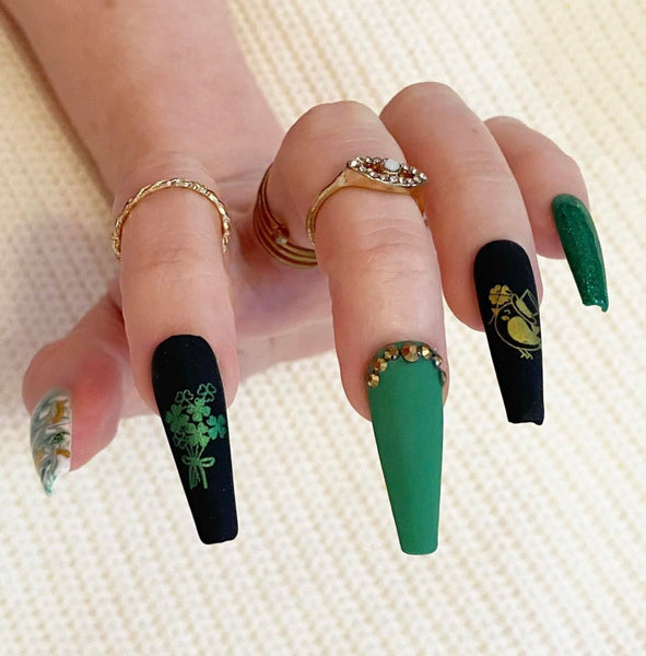 Load image into Gallery viewer, Hand wearing St Patrick's Day handmade false nails in green, black and gold with bird and shamrocks designs, rhinestones and glitter