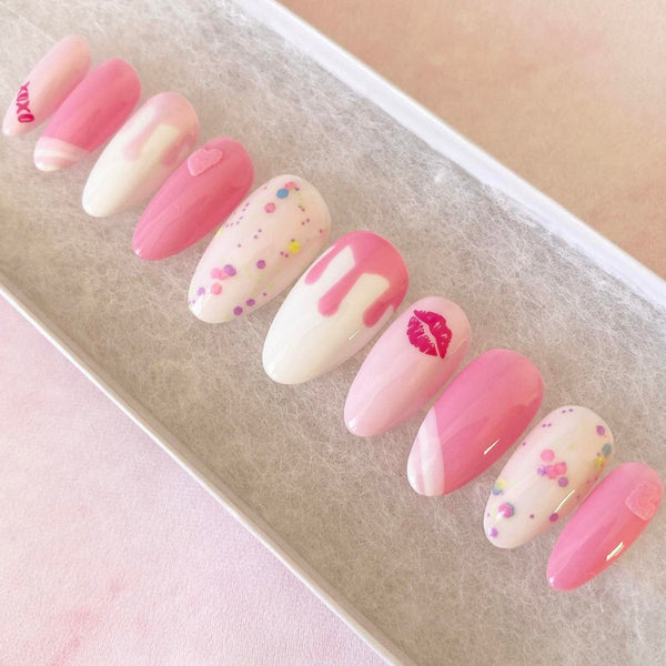 Load image into Gallery viewer, Short almond pink and white press-on nails with various shades of pink, featuring an xoxo and lips design, drip artwork, and 3D hearts all in pink, and confetti style glitter.