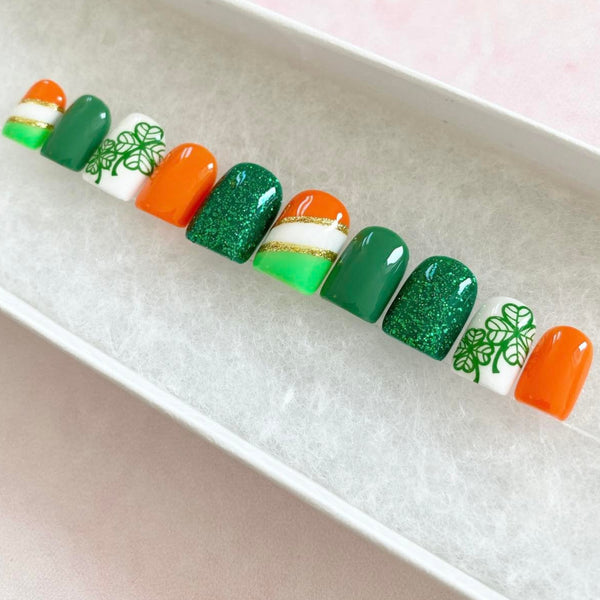 Load image into Gallery viewer, St Patrick's Day handmade false nails in green, orange, white and gold with lucky clover design and glitter, in a short square shape, from Illuminate by Liana