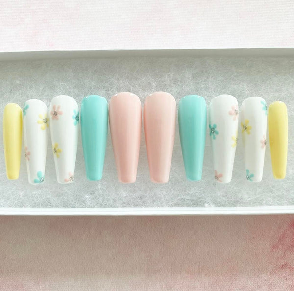 Load image into Gallery viewer, Long coffin press-on nails featuring a delicate floral design in pastel colours including yellow, blue, pink, and white, and a touch of silver glitter, created by Illuminate by Liana UK