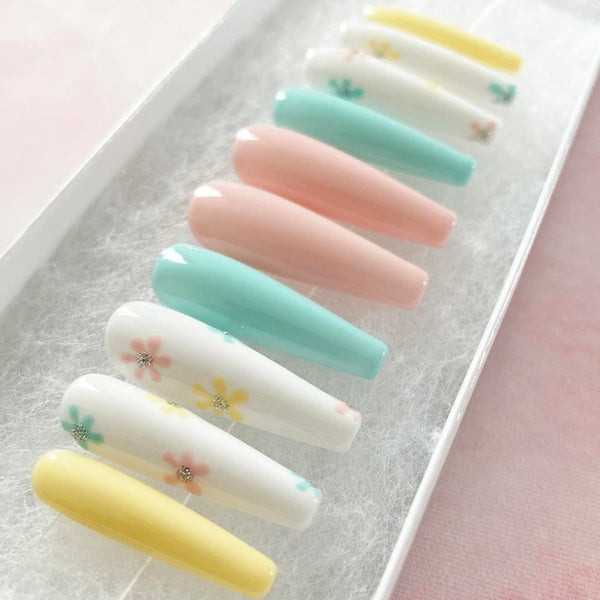 Load image into Gallery viewer, Long coffin press-on nails in pastel colours including yellow, blue, pink, and white, adorned with a floral design and a touch of silver glitter.