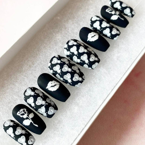 Load image into Gallery viewer, Short press-on nails in a black and white matte design with white roses, lips, and heart-shaped lollipops designs, in a short coffin shape.