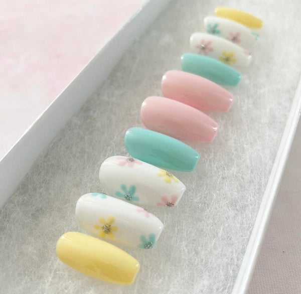 Load image into Gallery viewer, Short coffin handmade false nails in pastel colours including yellow, blue, pink, and white, adorned with a floral design and a touch of silver glitter at the centres of the flowers.
