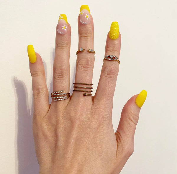 Load image into Gallery viewer, A hand wearing short coffin press-on nails featuring a yellow French tip design with a delicate daisy design and tiny white pearls, created by Illuminate by Liana
