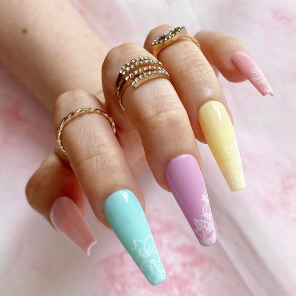 Load image into Gallery viewer, A hand wearing long coffin pastel press-on nails with a floral design and gold rings on a soft pink background