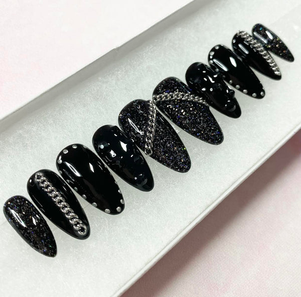 Load image into Gallery viewer, Handmade press-on nails in a black gothic or rock style, with silver chain embellishment, black rhinestones, glitter, and a silver chrome stud design, in a long almond shape.