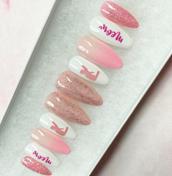 Load image into Gallery viewer, A set of handmade press-on nails featuring various designs including solid pink glitter, pink ombre gradients, solid pink ombre, white with pink cat silhouettes, and white with pink script text reading 'meow', in an almond shape, displayed in a white presentation box.