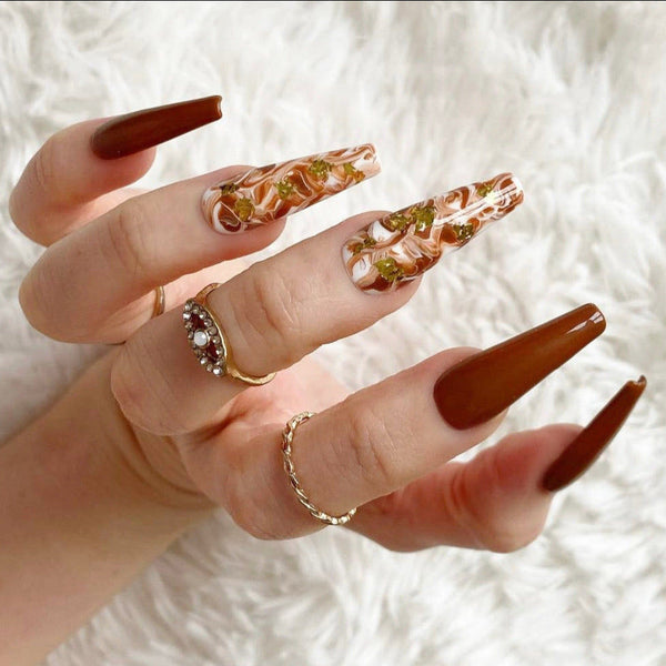 Load image into Gallery viewer, A hand wearing long coffin autumn press-on nails in brown, white and gold, featuring a marble design and gold leaf accents on two nails, against a soft white background.