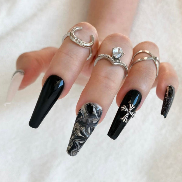 Load image into Gallery viewer, A hand wearing black-and-white gothic grunge style false nails in a long coffin shape featuring glitter, silver chains and silver cross gems, and a black-white marble effect, as well as silver rings on three fingers.