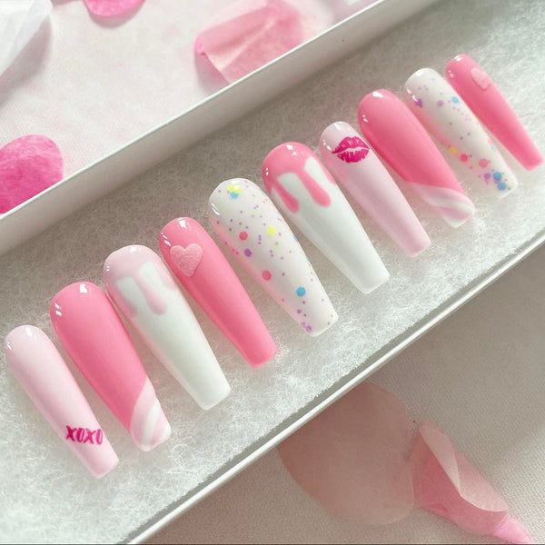 Load image into Gallery viewer, Pink and white press-on nails with various shades of pink, featuring an xoxo and lips design, drip artwork, and 3D hearts all in pink, and confetti style glitter, in a white presentation box with pink petals in the background.