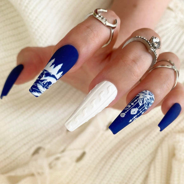 Load image into Gallery viewer, A hand wearing Christmas press-on nails featuring a blue and white Christmas snow scene design with reindeer and Christmas baubles, and a white 3D sweater design, as well as silver rings on the fingers.