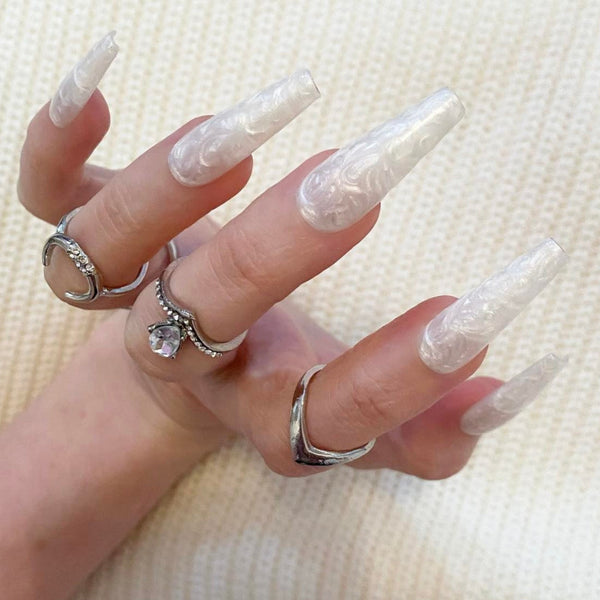 Load image into Gallery viewer, A hand wearing white pearl press on nails with a mother of pearl shimmer design, and silver rings on the fingers.