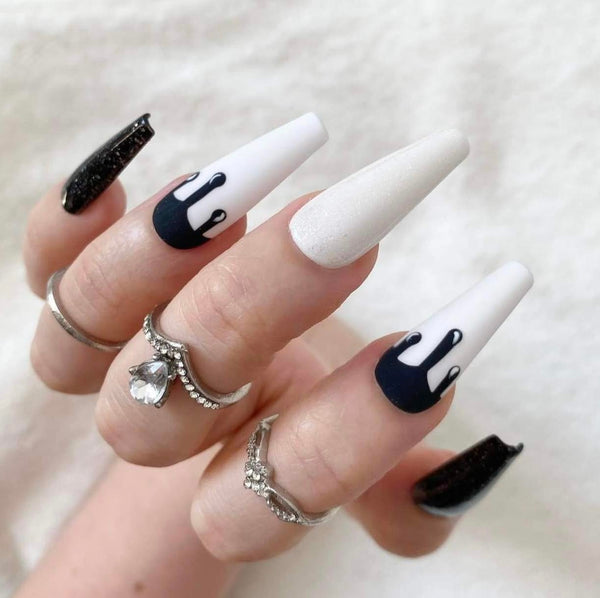 Load image into Gallery viewer, A close-up of a hand with long coffin-shaped nails featuring a white and black dripping paint design in a pop-art style, and subtle white and black glitter, styled with silver rings against a soft white background.