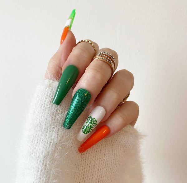 Load image into Gallery viewer, Hand showcasing St Patrick's Day handmade press-on nails in vivid greens, orange, and gold with a lucky clover design and glitter
