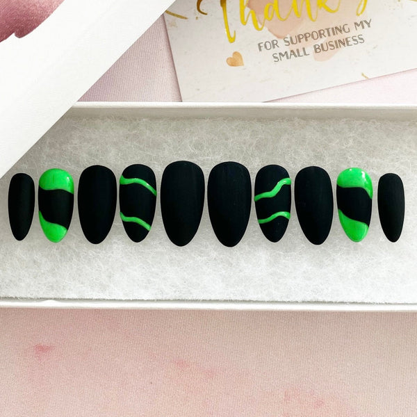 Load image into Gallery viewer, Short almond press-on nails in matte black with neon green wavy lines and abstract art on four of the nails, in a white presentation box.