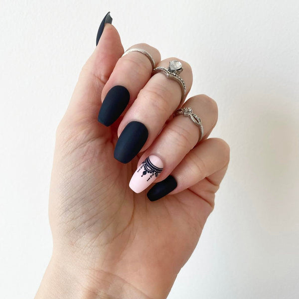 Load image into Gallery viewer, Hand wearing short coffin black and pink nails with a boho necklace design on the pink nail, wearing rings, against a white background.