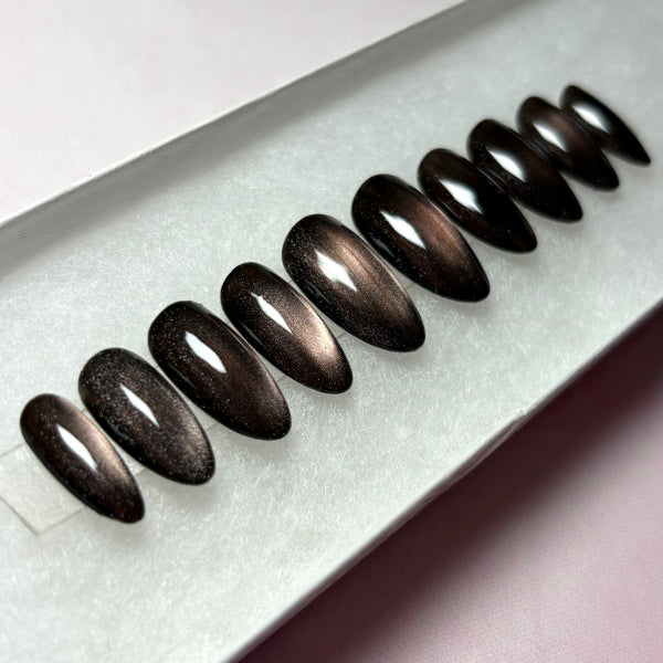 Load image into Gallery viewer, Cat eye press-on nails featuring a dark metallic cat-eye finish that shifts from burnished bronze to deep brown-black, in a short almond shape, displayed in a white presentation box.
