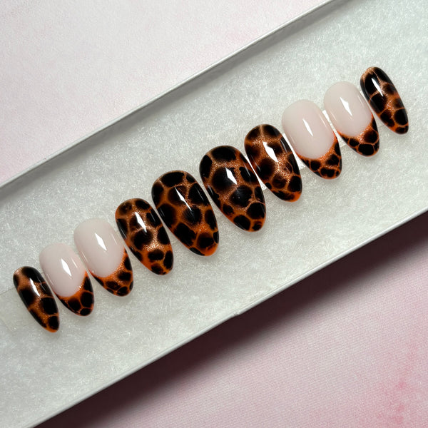 Load image into Gallery viewer, Handmade stick-on nails featuring an animal print design that resembles leopard print or tortoiseshell in copper and deep brown-black, as well as four French tip nails tipped with the same animal print pattern, displayed in a white presentation box.
