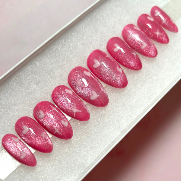 Load image into Gallery viewer, Short almond press-on nails in shimmery pink with white hearts and stars design.

