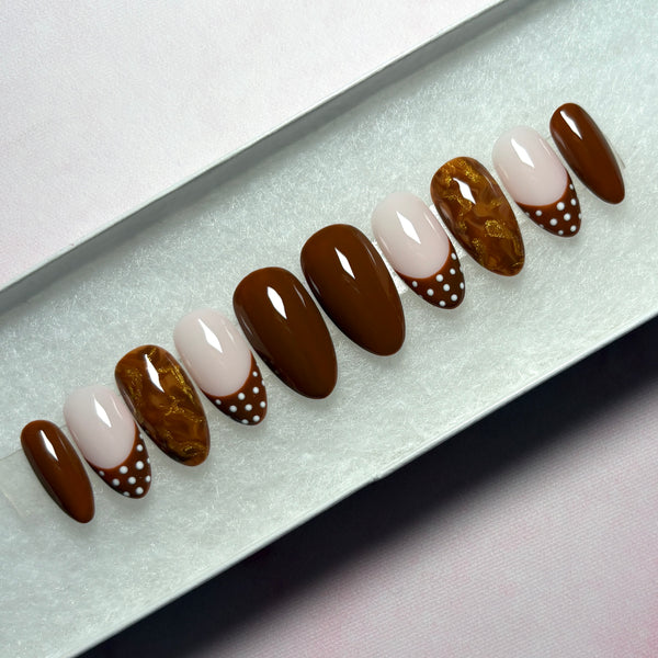Load image into Gallery viewer, A set of autumn stick-on nails in a short almond shape, in warm chocolate brown, featuring four solid brown nails, four French tip nails with chocolate-brown tips adorned with white polka dots, and two marble effect brown and metallic gold nails, displayed in a white presentation box.
