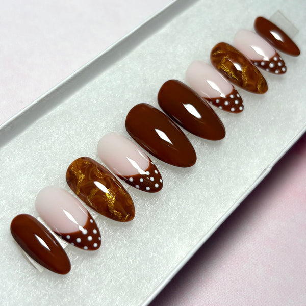 Load image into Gallery viewer, Autumn press-on nails in a warm chocolate brown, featuring four solid brown nails, four French tip nails with chocolate-brown tips adorned with white polka dots, and two marble effect brown and metallic gold nails, handmade by Illuminate by Liana Press-On Nails UK.
