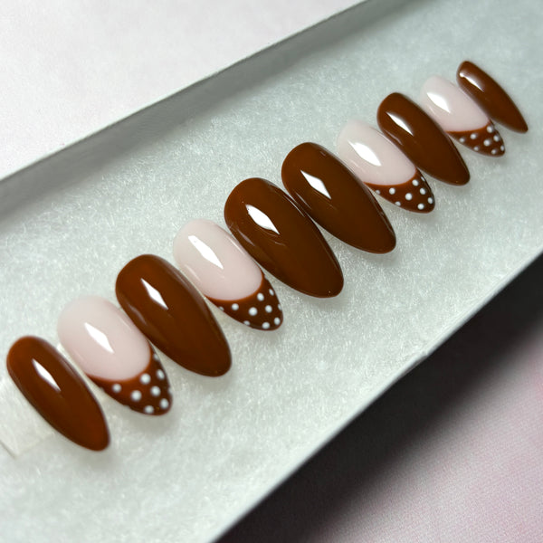 Load image into Gallery viewer, A set of autumn press-on nails in deep chocolate-brown, featuring four brown French tip nails with white polka dots on the tips, and six glossy brown nails, in a short almond shape, displayed in a white presentation box.
