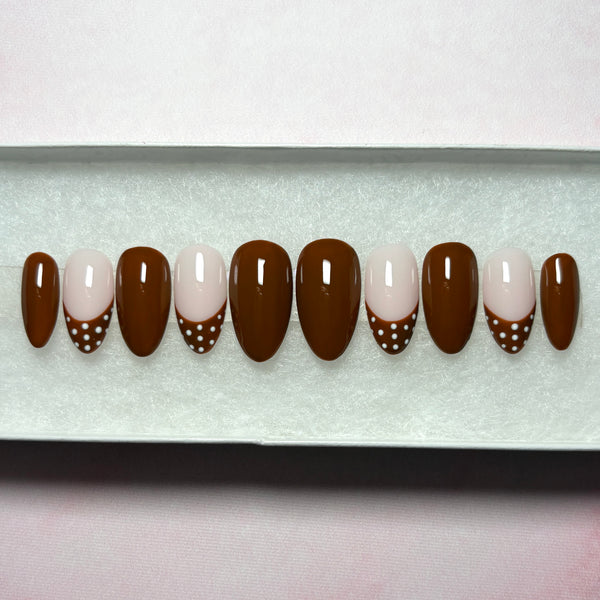 Load image into Gallery viewer, Stick-on nails in deep chocolate-brown, featuring four brown French tip nails with white polka dots on the tips, and six glossy brown nails, in a short almond shape, displayed in a white presentation box.
