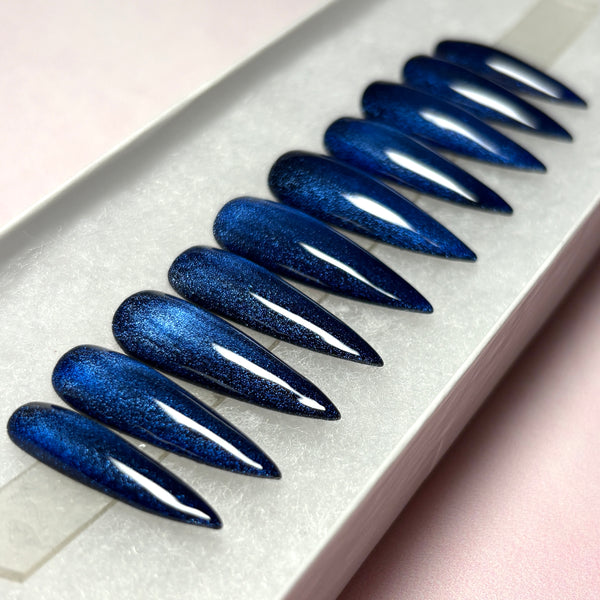 Load image into Gallery viewer, Blue cat-eye press-on nails that colour-shift from dark blue through black, handmade in a long stiletto shape displayed in a white presentation box
