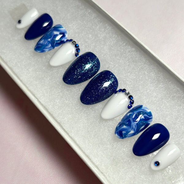 Load image into Gallery viewer, Blue and white press-on nails in various shades of blue and white, decorated with dainty blue and silver rhinestone gems, blue glitter and a marble effect, created by Illuminate by Liana UK. 
