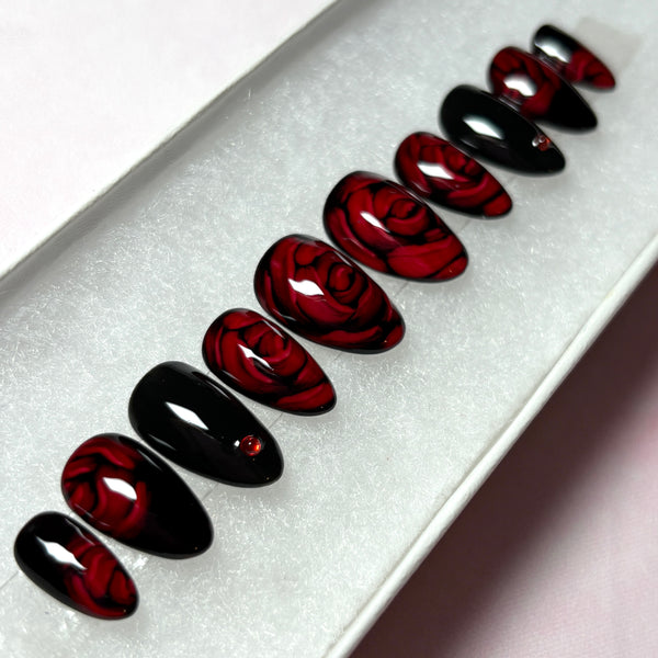 Load image into Gallery viewer, Red and black press-on nails featuring 3D effect deep red roses and delicate red rhinestones, in a short almond shape, displayed in a white presentation box.
