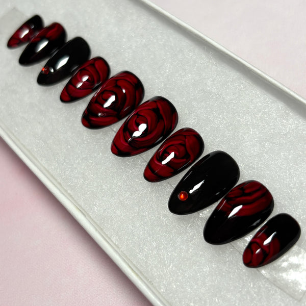 Load image into Gallery viewer, Gothic vibe red and black press-on nails with 3D effect roses in dark red and delicate red rhinestones, in a short almond shape, created by Illuminate by Liana UK.
