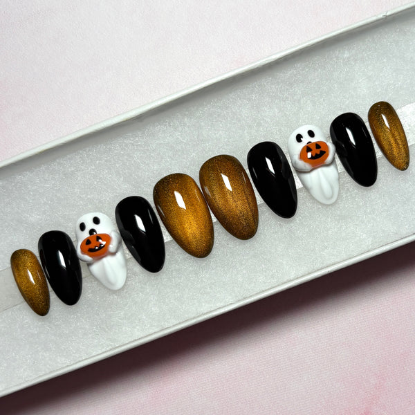 Load image into Gallery viewer, Halloween false nails in a short almond shape, featuring glossy black, metallic coppery gold, and white 3D ghost designs holding tiny 3D orange jack-o'-lantern pumpkins, displayed in a white presentation box.
