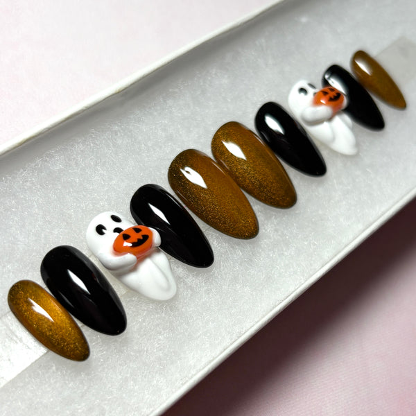 Load image into Gallery viewer, Short almond Halloween false nails featuring glossy black, metallic coppery gold, and white 3D ghost designs holding tiny 3D orange jack-o'-lantern pumpkins, displayed in a white presentation box.
