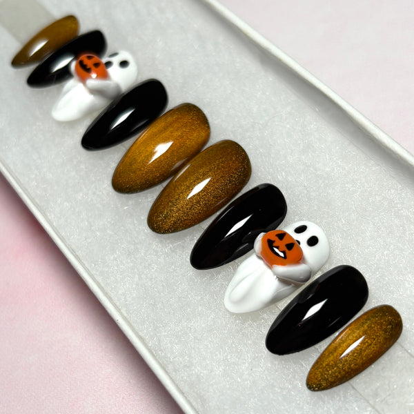 Load image into Gallery viewer, A set of Halloween-themed press-on featuring glossy black, metallic coppery gold, and white 3D ghost designs holding tiny 3D orange jack-o'-lantern pumpkins, displayed in a white presentation box.
