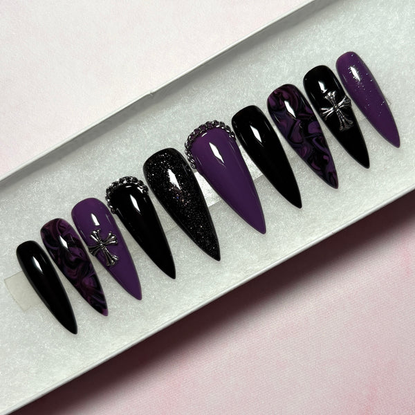 Load image into Gallery viewer, A set of long false nails featuring a gothic design in black and deep purple with a black-purple marble effect, subtle black and purple glitter, and 3D silver chain and cross embellishments, displayed in a white presentation box.
