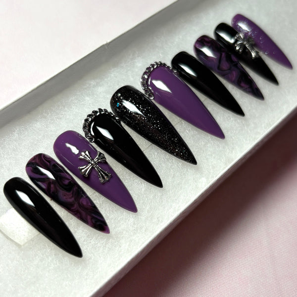 Load image into Gallery viewer, Gothic style press-on nails in a long stiletto shape, featuring a black and deep purple design with a black-purple marble effect, subtle black and purple glitter, and 3D silver chain and cross embellishments, handmade by Illuminate by Liana Press-On Nails UK.
