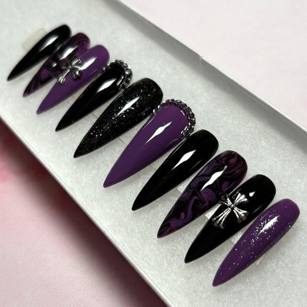 Load image into Gallery viewer, Gothic style handmade false nails in a long stiletto shape, featuring a black and deep purple design with a black-purple marble effect, subtle black and purple glitter, and 3D silver chain and cross embellishments, displayed in a white presentation box.
