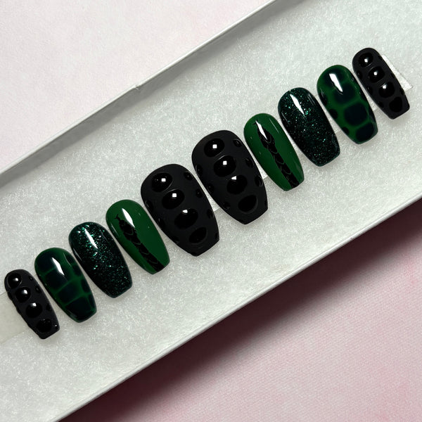 Load image into Gallery viewer, A set of short coffin press-on nails in black and dark green, featuring a black snake design on a green background, snake print effect as 3D scales effect as well as subtle green glitter, displayed in a white presentation box.
