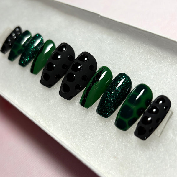 Load image into Gallery viewer, A set of short coffin press-on nails with a gothic vibe, in black and deep emerald green, featuring a black snake design on a green background, snake print effect as 3D scales effect as well as subtle green glitter, displayed in a white presentation box.
