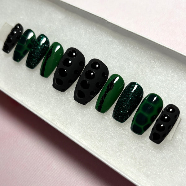 Load image into Gallery viewer, Handmade false nails in black and deep emerald green, featuring a black snake design on a green background, snake print effect as 3D scales effect as well as subtle green glitter, displayed in a white presentation box.
