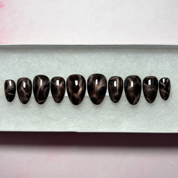 Load image into Gallery viewer, A set of handmade press-on nails in black and bronze brown cat eye that shimmers and glitters, giving a leopard print or tortoise shell effect, in a short almond shape, displayed in a white presentation box. 
