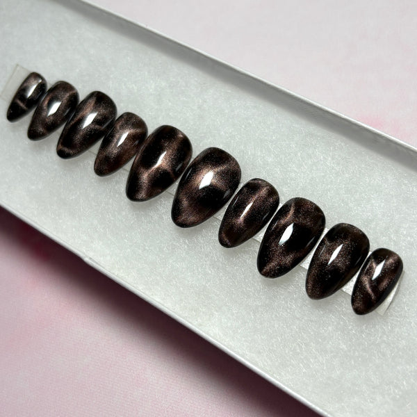 Load image into Gallery viewer, Handmade cat eye false nails in black and bronze brown cat eye that shimmers and glitters, giving a leopard print or tortoise shell effect, in a short almond shape, displayed in a white presentation box. 
