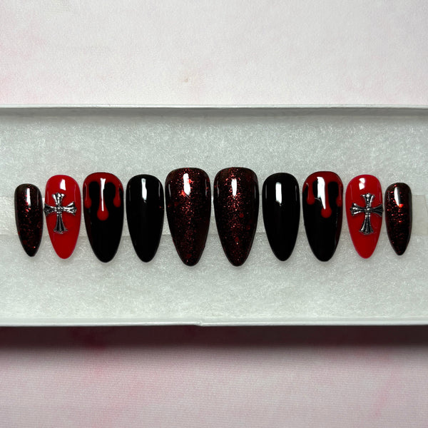 Load image into Gallery viewer, Gothic goth grunge stick-on nails in red and black featuring deep red blood drips on two black nails, 3D metallic silver cross gems on two red nails, deep red glitter on four nails, and two solid black nails, in a long almond shape, displayed in a white presentation box.
