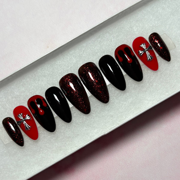 Load image into Gallery viewer, Gothic goth grunge handmade false nails in red and black featuring deep red blood drips on two black nails, 3D metallic silver cross gems on two red nails, deep red glitter on four nails, and two solid black nails, in a long almond shape, displayed in a white presentation box.
