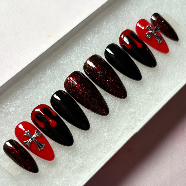 Load image into Gallery viewer, Gothic goth grunge press-on nails in red and black featuring deep red blood drips on two black nails, 3D metallic silver cross gems on two red nails, deep red glitter on four nails, and two solid black nails, in a long almond shape, displayed in a white presentation box.
