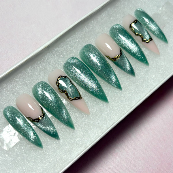Load image into Gallery viewer, Long stiletto press-on nails in shimmering green cat eye with delicate gold chrome accents, in a white presentation box.
