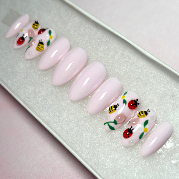 Load image into Gallery viewer, Pastel pink false nails with 3D ladybirds, bees and flowers artwork, in a short almond shape, displayed in a white presentation box.
